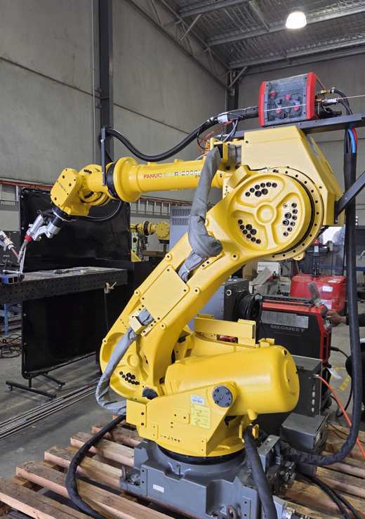 Refurbished FANUC R-2000iA robot arm with welding torch on a welding table