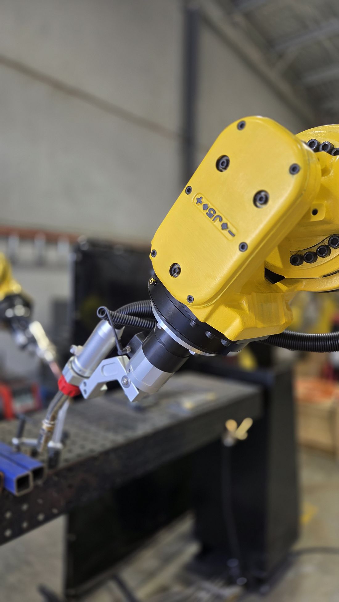 The welding torch and wire on the robot wrist, over the welding bench
